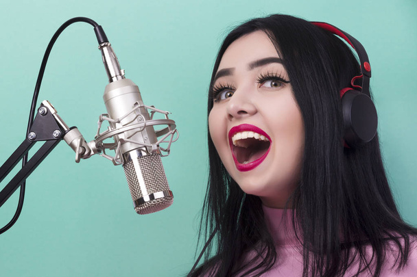 girl with red lips singing to the microphone in a studio on azure background - 写真・画像