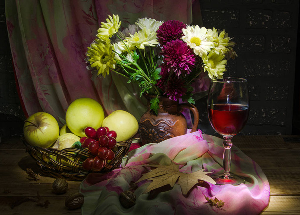 still life from bouquet of chrysanthemum with apples in basket and wine in dark - Foto, Imagem
