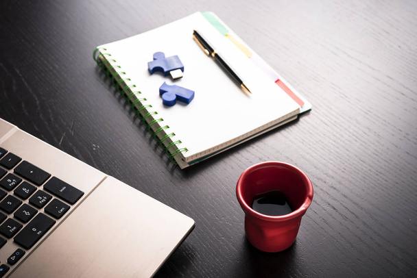 Натюрморт с блокнотом, ноутбуком, ручкой и красной чашкой кофе над черным столом офиса. Символ работы
 - Фото, изображение