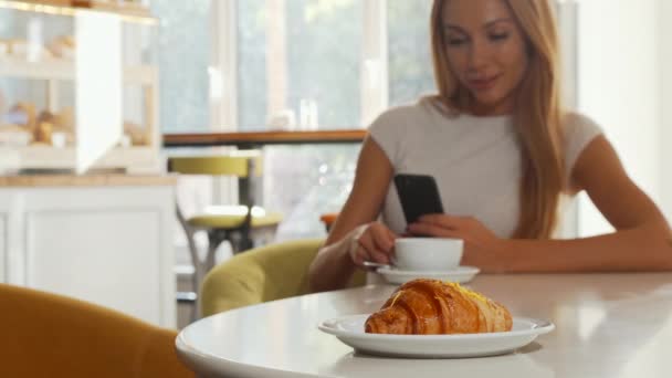 Foco seletivo em croissant saboroso, mulher usando telefone inteligente no café
 - Filmagem, Vídeo