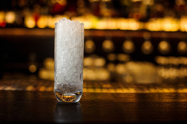 High transparent glass filled with ice cubes on the bar counter of restaurant in blurred background - Fotografie, Obrázek