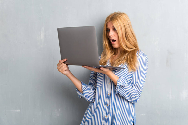 Blondes Mädchen mit Laptop auf strukturiertem Grunge-Hintergrund - Foto, Bild