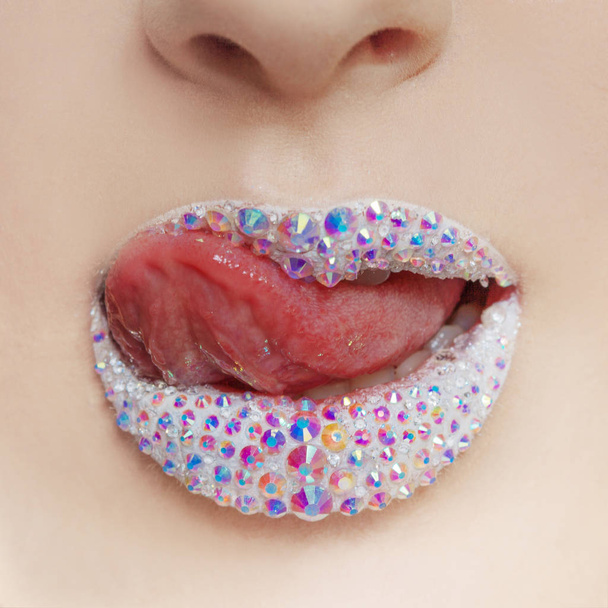 shining lips covered with rhinestones. Beautiful woman with white lipstick on her lips, Tongue licks lips - Photo, image