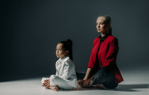 Joven madre con su hija pequeña están sentados en el suelo en sukhasana pose de yoga
. - Foto, imagen