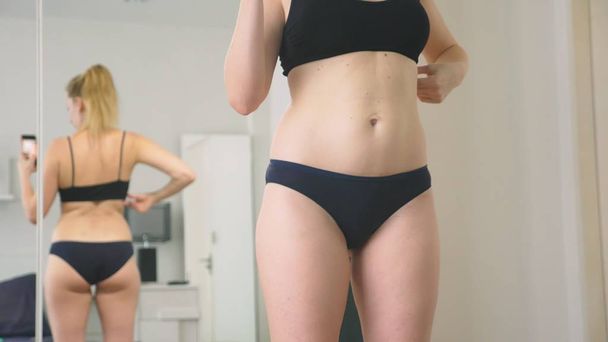 The concept of overweight and weight loss. A woman looks at herself in the mirror and photographs her figure. to compare the results before and after losing weight. - Zdjęcie, obraz