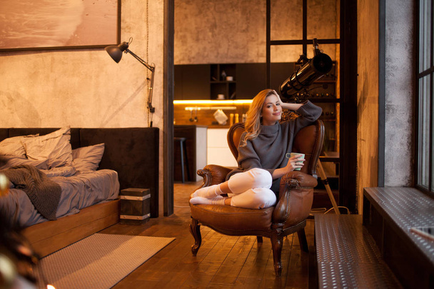 belle et confiante jeune blonde est assise dans une chaise confortable dans son appartement
. - Photo, image