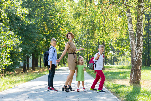 Счастливая молодая семья, мама с тремя детьми гуляет в парке. Понятие здорового образа жизни
 - Фото, изображение