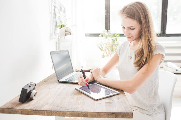 Young business woman working at home and draws on the tablet. Creative Scandinavian style workspace - 写真・画像