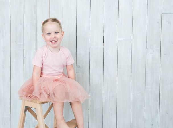 Χαριτωμένο μικρό ξανθό κορίτσι που κάθεται σε μια καρέκλα σε λευκό φόντο. - Φωτογραφία, εικόνα
