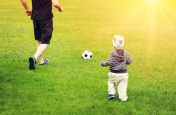 Little boy playting football with father on the field with gates. Active man and child in summer with ball - Φωτογραφία, εικόνα