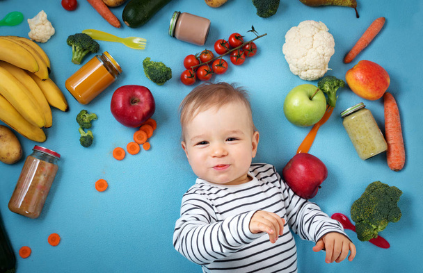 baby surrounded with fruits and vegetables on blue blanket, healthy child nutrition - Foto, Bild