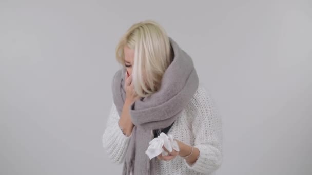 Sick blond woman in a knitted warm scarf sneezes over white background.  - Záběry, video