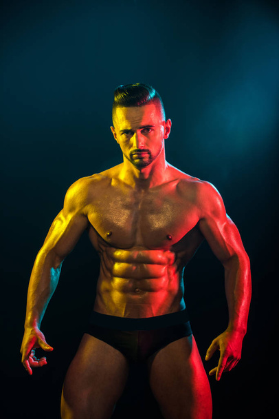 Ισχυρή Αθλητικός άνδρας δείχνει μυώδες σώμα και sixpack abs σε σκούρο φόντο. Σέξι closeup πορτρέτο του όμορφος τόπλες αρσενικό μοντέλο με όμορφο σώμα. Δύναμη και κίνητρο - Φωτογραφία, εικόνα