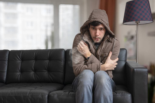 Mężczyzna siedzi na kanapie w domu i uczucie zimna. - Zdjęcie, obraz