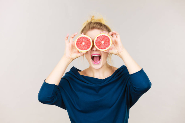 Healthy diet, refreshing food full of vitamins. Woman holding sweet delicious citrus fruit, grapefruit two halfs pretending it is eyeglasses - Foto, Bild
