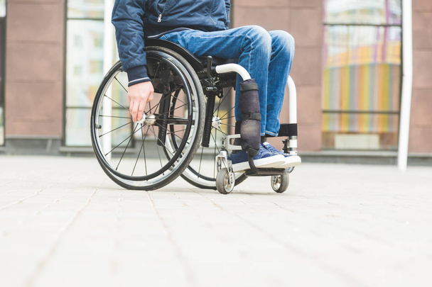 Young man in a wheelchair against the backdrop of a modern high-rise building. - Photo, Image