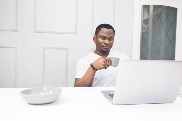 Jeune homme d'affaires afro-américain travaillant sur un ordinateur portable dans la cuisine dans un intérieur moderne
. - Photo, image