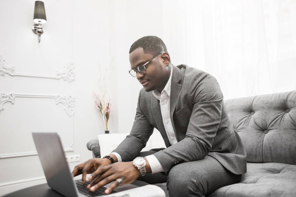 Young African American businessman in a gray suit working behind a laptop. - Fotó, kép