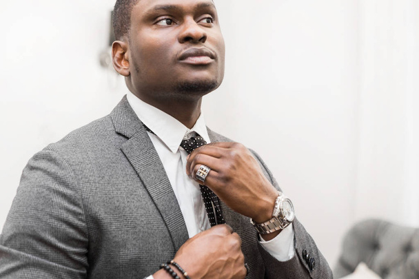 Young African American businessman in a gray suit tying a tie on a white background. - Foto, Imagem