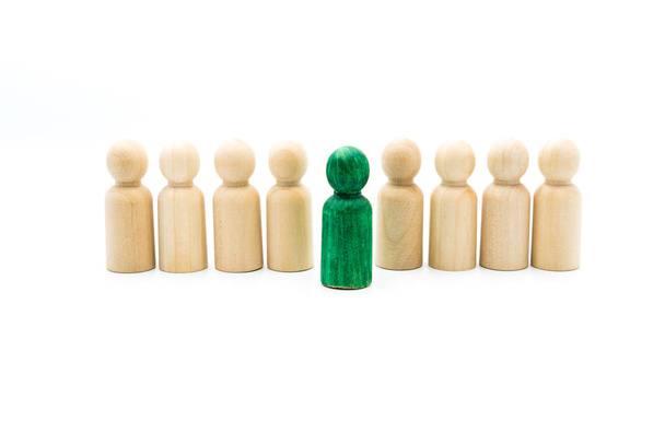 Holzfiguren reihen sich als Business-Team aneinander, wobei eine grüne Figur aus der Menge heraussticht, isoliert auf weißem Hintergrund. Konzeptionelles Bild des Andersseins - Foto, Bild