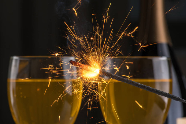 Burning sparkler on the background of glasses of wine, a lot of sparks - Photo, image