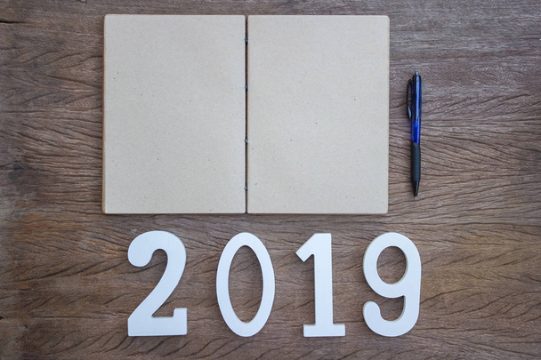 あなたの仕事の計画の概念に焦点を合わせる: トップ ビュー、フラット横たわっていたメモ帳と木製のテーブルでカット木材番号 2019 のペン。新年の解像度背景の個人作業スペース。新しい年の人生計画コンセプト. - 写真・画像