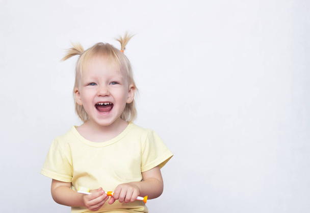 Little blue-eyed blonde girl holding a toothbrush in her hand and laughing with an open mouth on a white background, copy space, beautiful - Fotografie, Obrázek