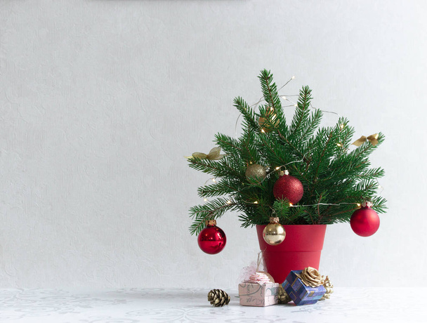 on a light background there is a Christmas decorated tree in a red pot under it - Fotoğraf, Görsel