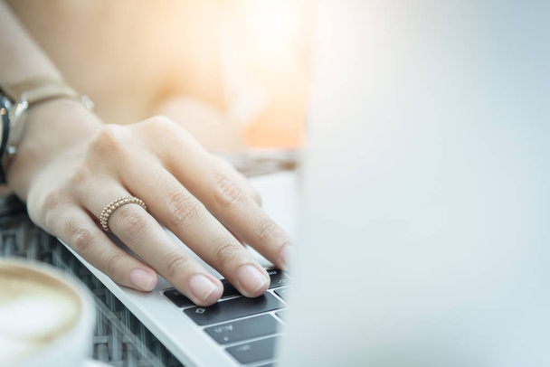 Азиатская женщина руки и женатое кольцо имеет прикосновения и печатание на ноутбуке компьютер с размытым кофе, компьютер и вид из окна. - Фото, изображение