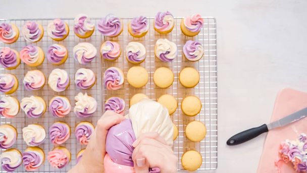 Flat lay. Piping pink and purple buttercream frosting on small vanilla cupcakes. - Photo, Image