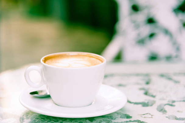 Біла чашка кави і срібна ложка, готова до подачі вранці з розслаблюючим і жовтим освітленням фону боке
. - Фото, зображення