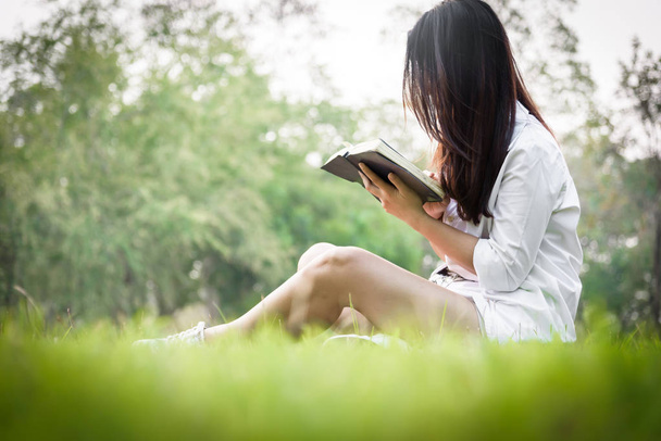 Gyönyörű ázsiai nő olvas egy könyvet a kertben boldogsággal és pihentető este naplementekor. - Fotó, kép