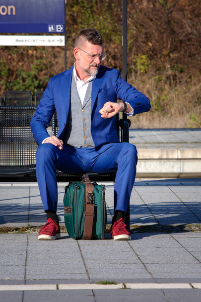 man in suit at train station looking annoyed at his wristwatch - 写真・画像
