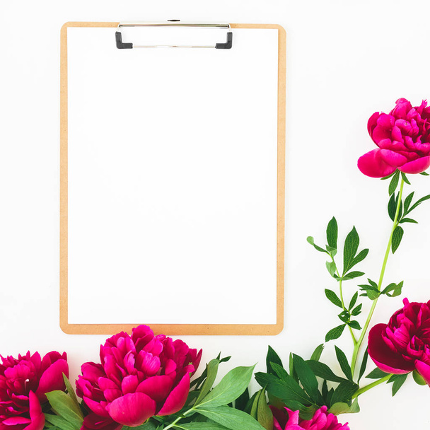 Frame van pioenrozen bloemen en Klembord met kopie ruimte op witte achtergrond. Plat lag, top uitzicht - Foto, afbeelding