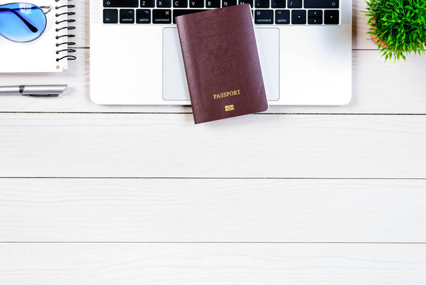 A munkavállaló és a munkavállaló íróasztal utazás álmodik, és készül az utazás és utazás a világ minden tájáról laptop és útlevél fehér fa asztal lapos felülnézetből. - Fotó, kép