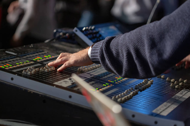 Soundman working on the mixing console behind the concert crowd. The hand moves one slider. - Photo, Image