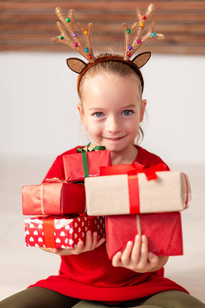 Cute young girl holding stack of christmas presents, smiling and looking at camera. Happy kid at christmas time. - Fotoğraf, Görsel