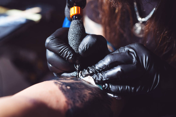     Close up tattoo machine. Man creating picture on hand with it in salon  - 写真・画像