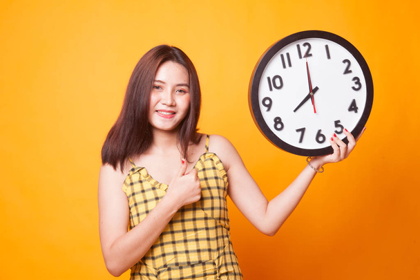 Jeune femme asiatique pouces vers le haut avec une horloge sur fond jaune
 - Photo, image