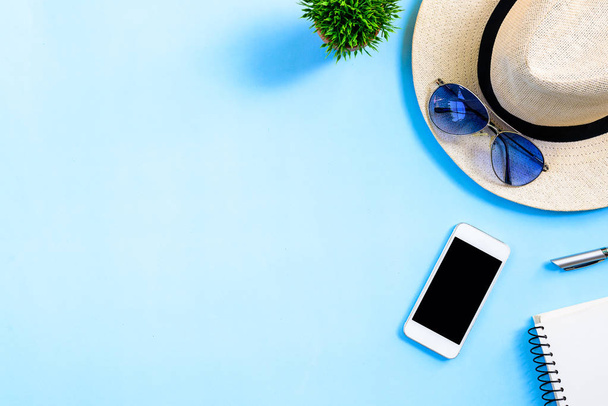 Top view summer travel planning concept with white hat, blue eyeglasses, phone and notebook copy space isolated on blue background. - Foto, Imagen
