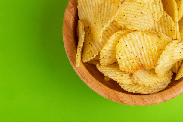 Crunchy corrugated potato chips in wooden bowl on bright green background. Junk food. Copy space - Fotografie, Obrázek