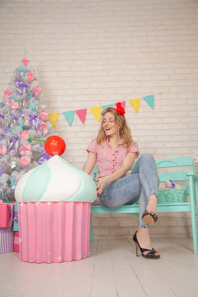 cute smiling woman in jeans and plaid shirt posing with giant pink cake and having fun on Christmas Tree Background - Foto, imagen