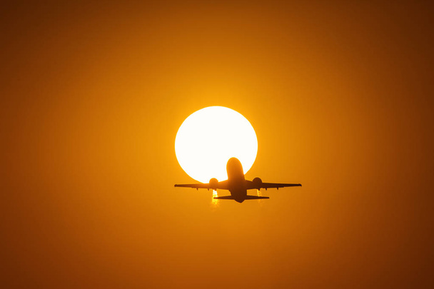 Silhouette of an air plane over the sun with beautiful red clouds in background - Photo, Image