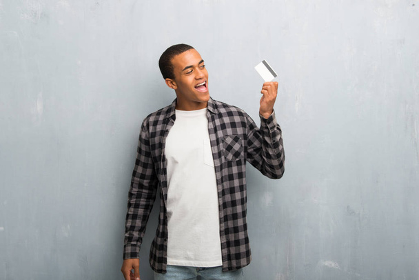 Giovane uomo afroamericano con camicia a scacchi in possesso di una carta di credito e pensando
 - Foto, immagini