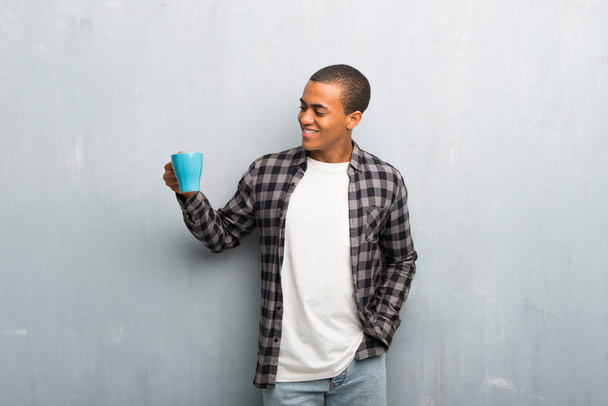 Young african american man with checkered shirt taking a coffee and smiling because he will start the day well - Foto, Imagem