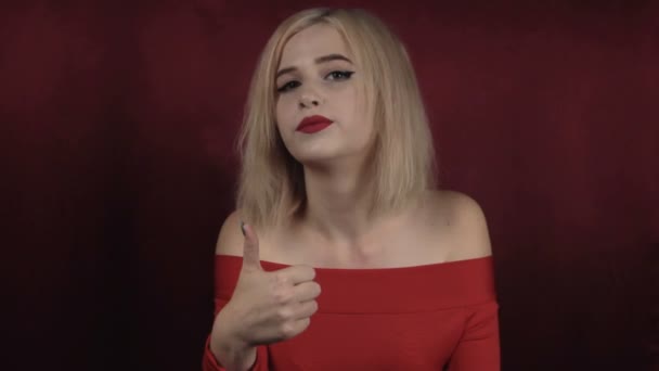 Happy beautiful girl shows hand, sign ok against the background of red rocking fabric. - Footage, Video