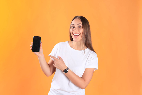 Young woman dressed in basic clothing isolated on yellow background, using mobile phone. - Фото, изображение