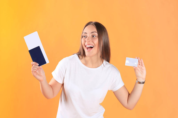 Excited young woman tourist standing isolated on yellow background holding passport with tickets, plastic credit card. - Foto, Imagem