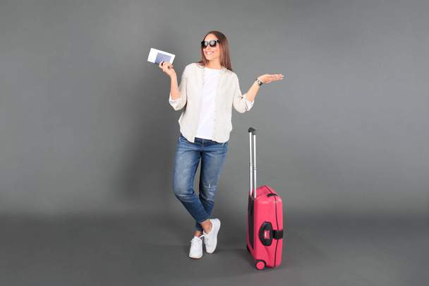 Young tourist girl in summer casual clothes, with sunglasses, red suitcase, passport, tickets isolated grey background - Foto, immagini