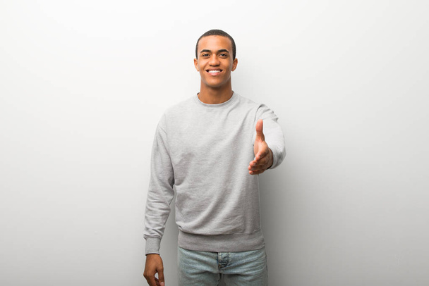 Hombre afroamericano sobre fondo blanco de pared estrechando las manos para cerrar una buena oferta
 - Foto, imagen